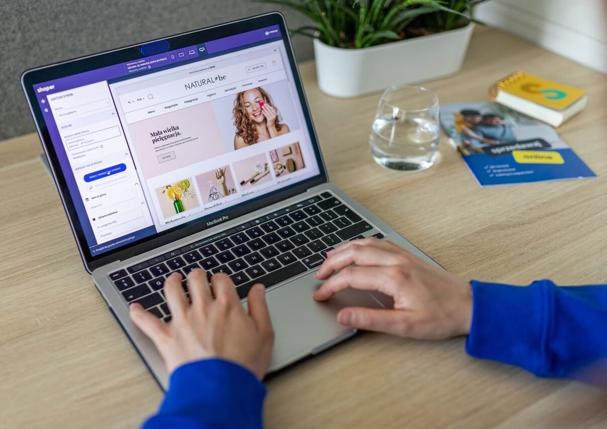 Hands typing on a laptop showing an e-commerce website in a modern office setting.